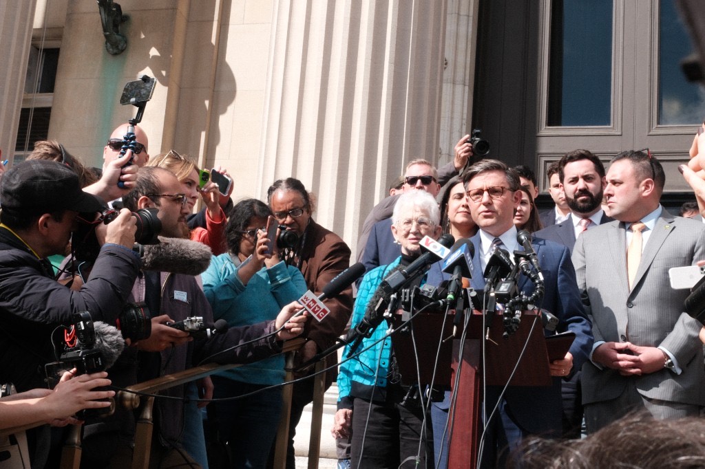 House Speaker Mike Johnson speaks at a podium surrounded by press and lawmakers on the steps of Low Library