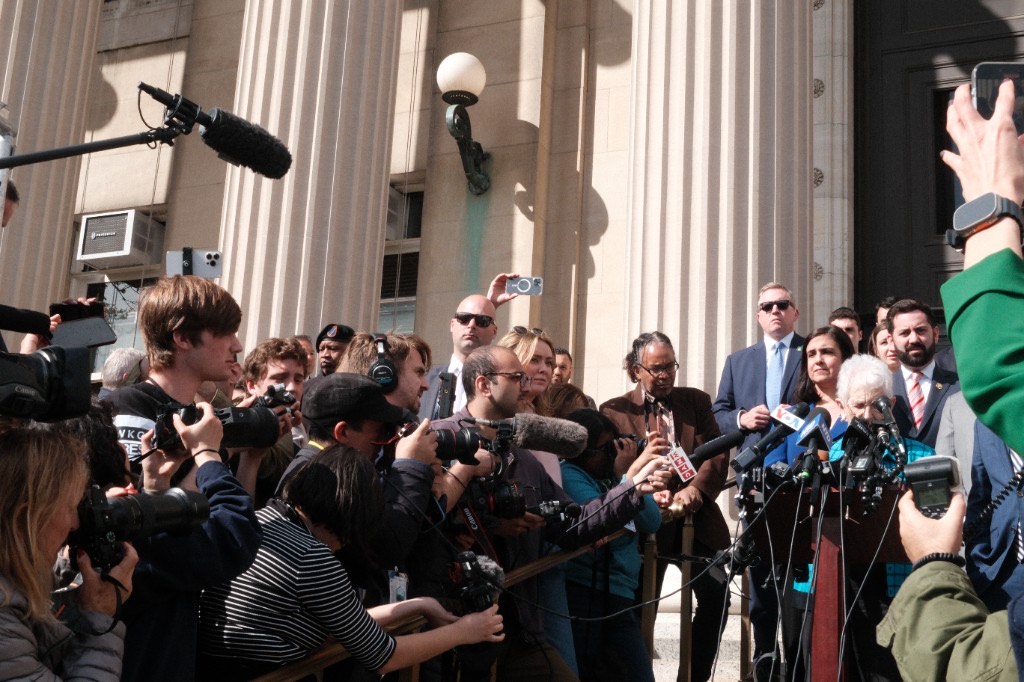 Wide view of the press conference showing the media crush at the podium