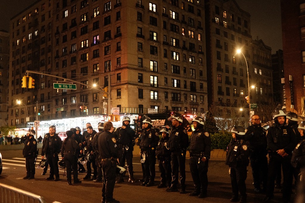 A line of NYPD officers standing in formation at W 116th Street at night